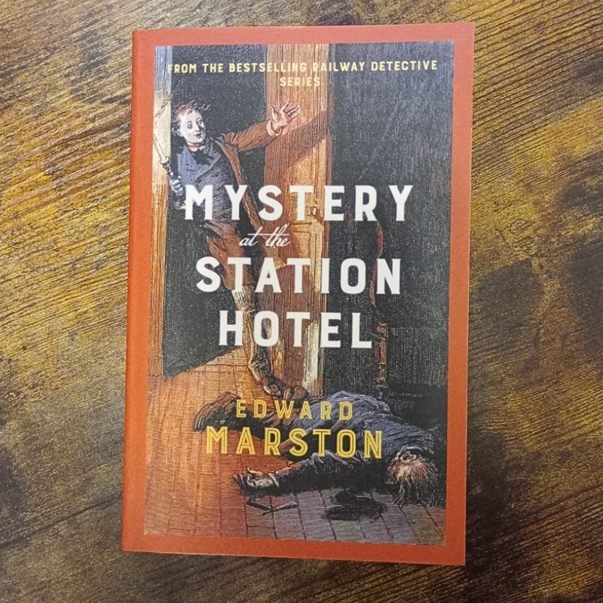 Book cover of 'Mystery at the Station Hotel' by Edward Marston on a wooden surface