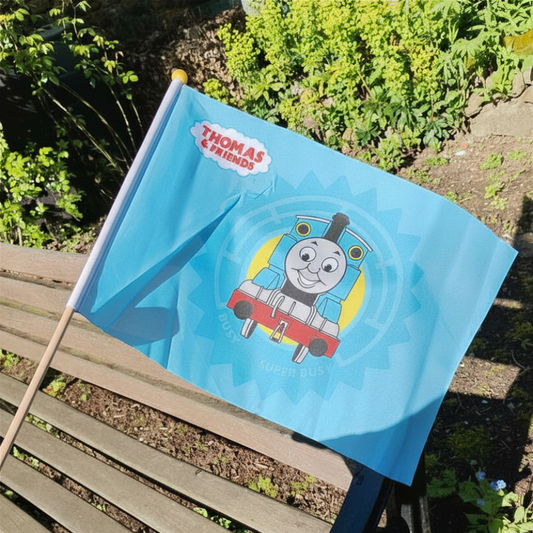 Blue flag with Thomas the Tank Engine design on a wooden bench outdoors.