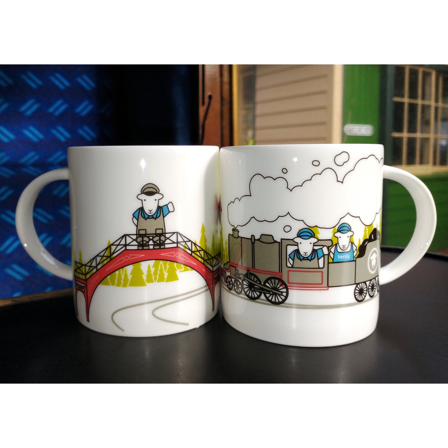 Two mugs together which show the full scene thay runs around the mug. Herdy the Sheep is waving from the top of the red footbridge and there are two Herdies on the locomotive.