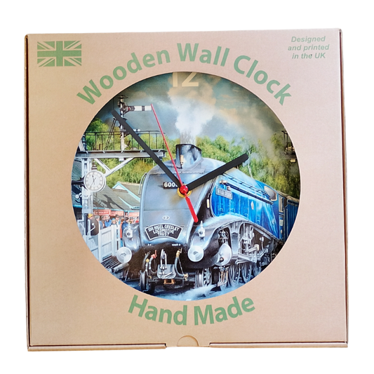 A wooden wall clock in its original packaging, featuring a circular cutout with a printed image of a steam train. The packaging is brown card with green text reading 'Wooden Wall Clock' and 'Hand Made'.