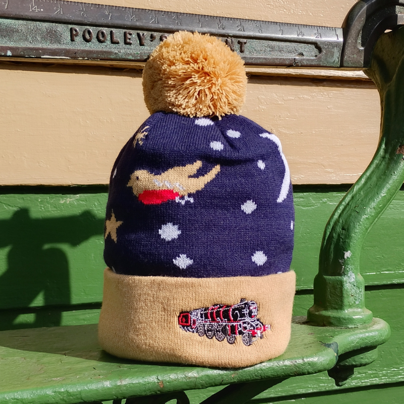 A knitted bobble hat in navy with a robin and snowflakes. With a honey coloured trim and bobble. Trim features an embroidered locomotive.