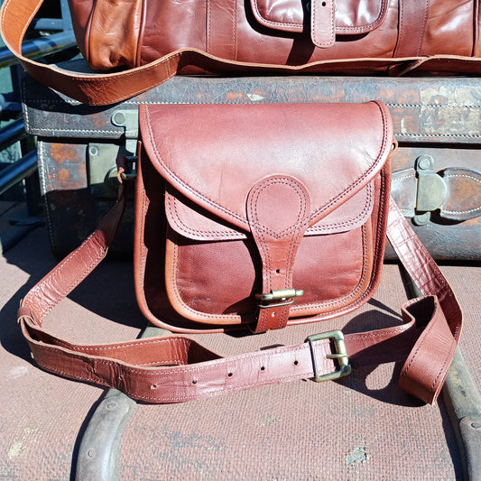 A chestnut brown coloured leather saddle bag with buckle fastening on both the bag closure and strap adjustment.