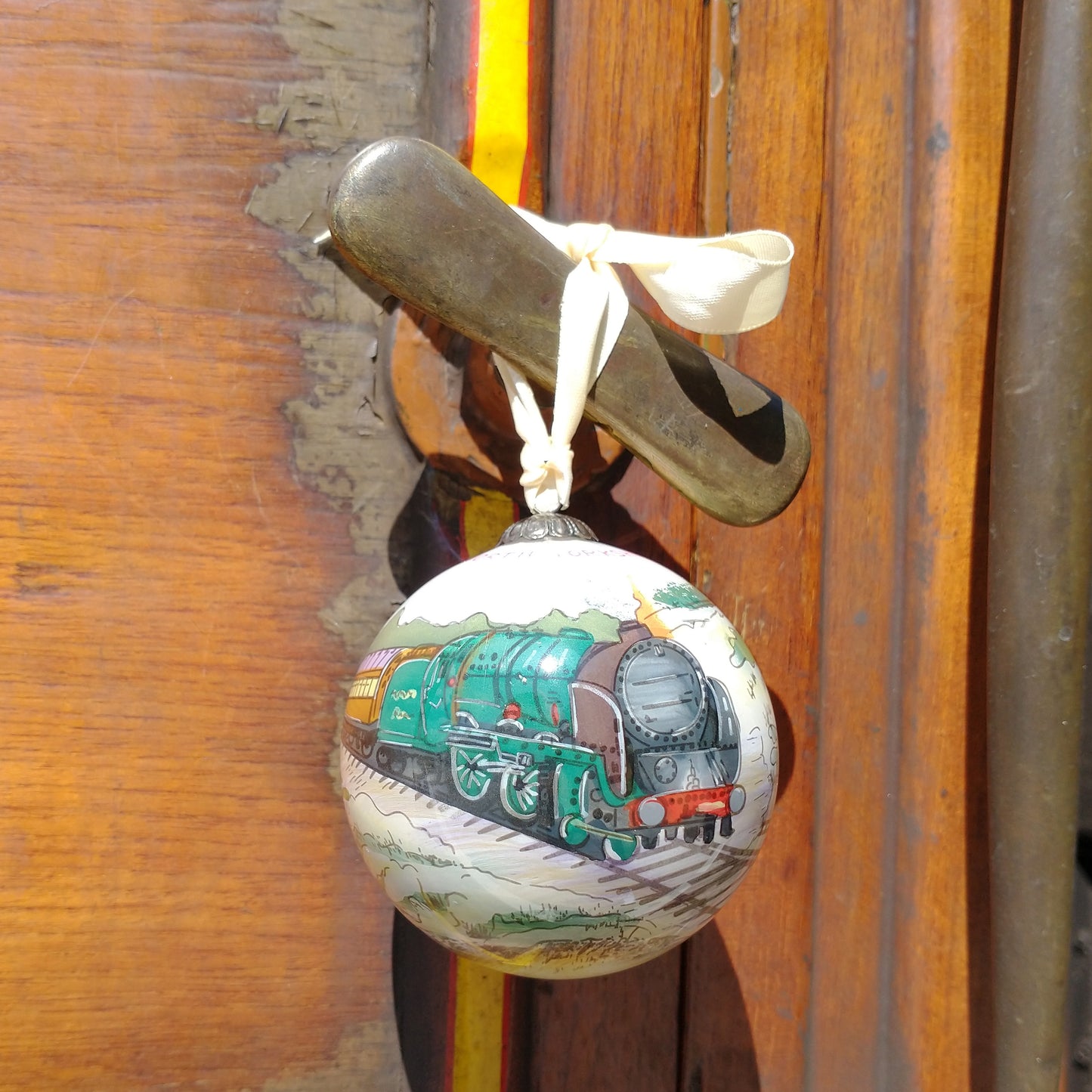 The bauble is tied to the handle of a teak carriage by a cream ribbon.