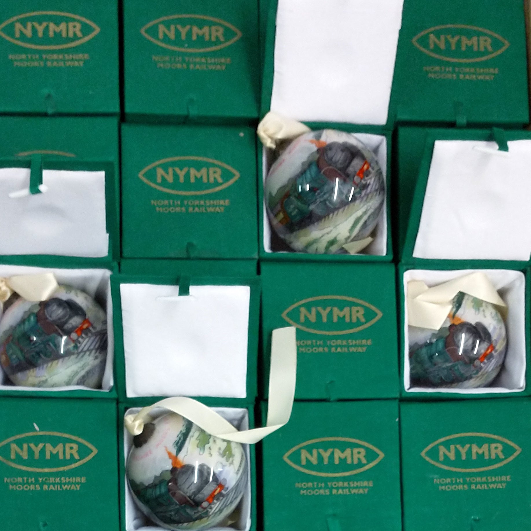 Boxes of baubles lined up in rows, the lids printed in gold with the NYMR logo. some of the boxes are opened up to show the baubles inside.