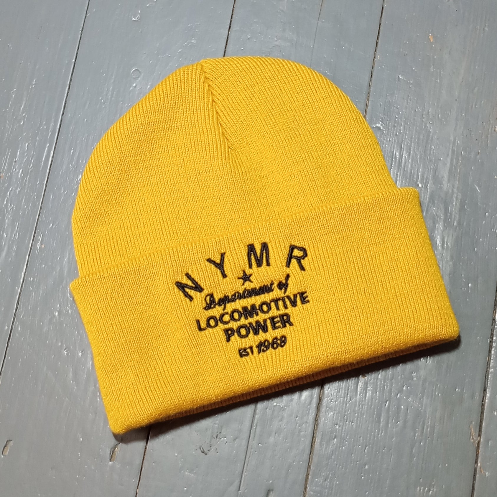 The mustard coloured beanie with black embroidery on the frontfold