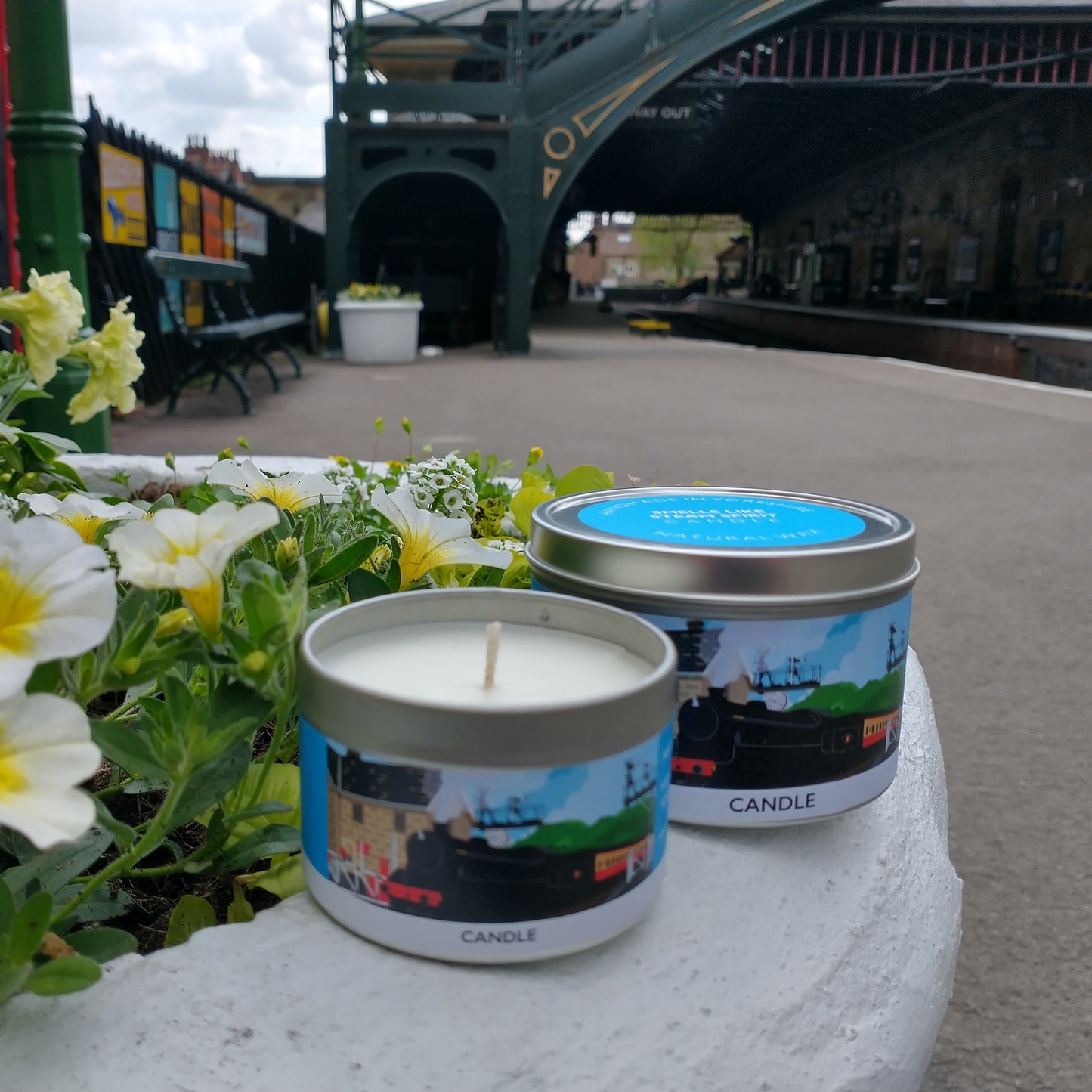 Two candles in tins posing on a station platform.