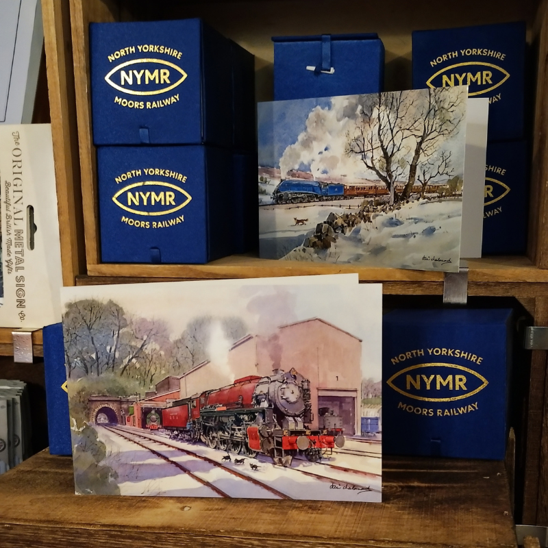 The cards shown on shelves surrounded by NYMR merch. They are landscape orientation and are folded at the left side, opening to the right.