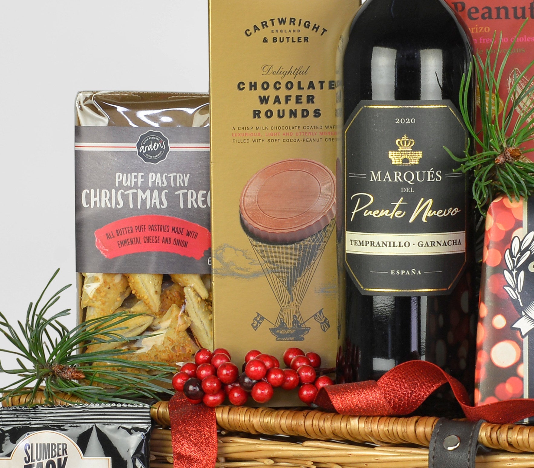 Gift basket with wine, snacks, Christmas tree puff pastries, surrounded by festive decorations.