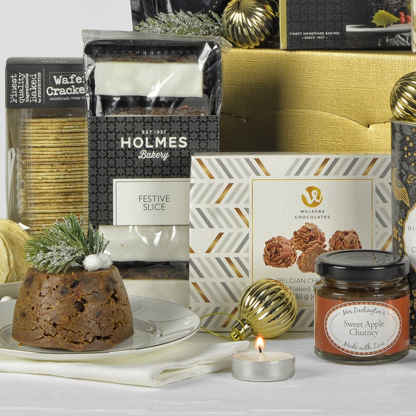 Assorted holiday treats including a plum pudding, candles, and gift boxes on a white surface.
