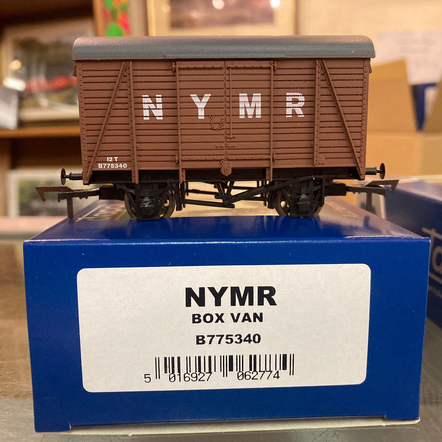 a model railway wagon with brown plank sides and a grey curved roof with standard couplings. NYMR is printed on the side in white.