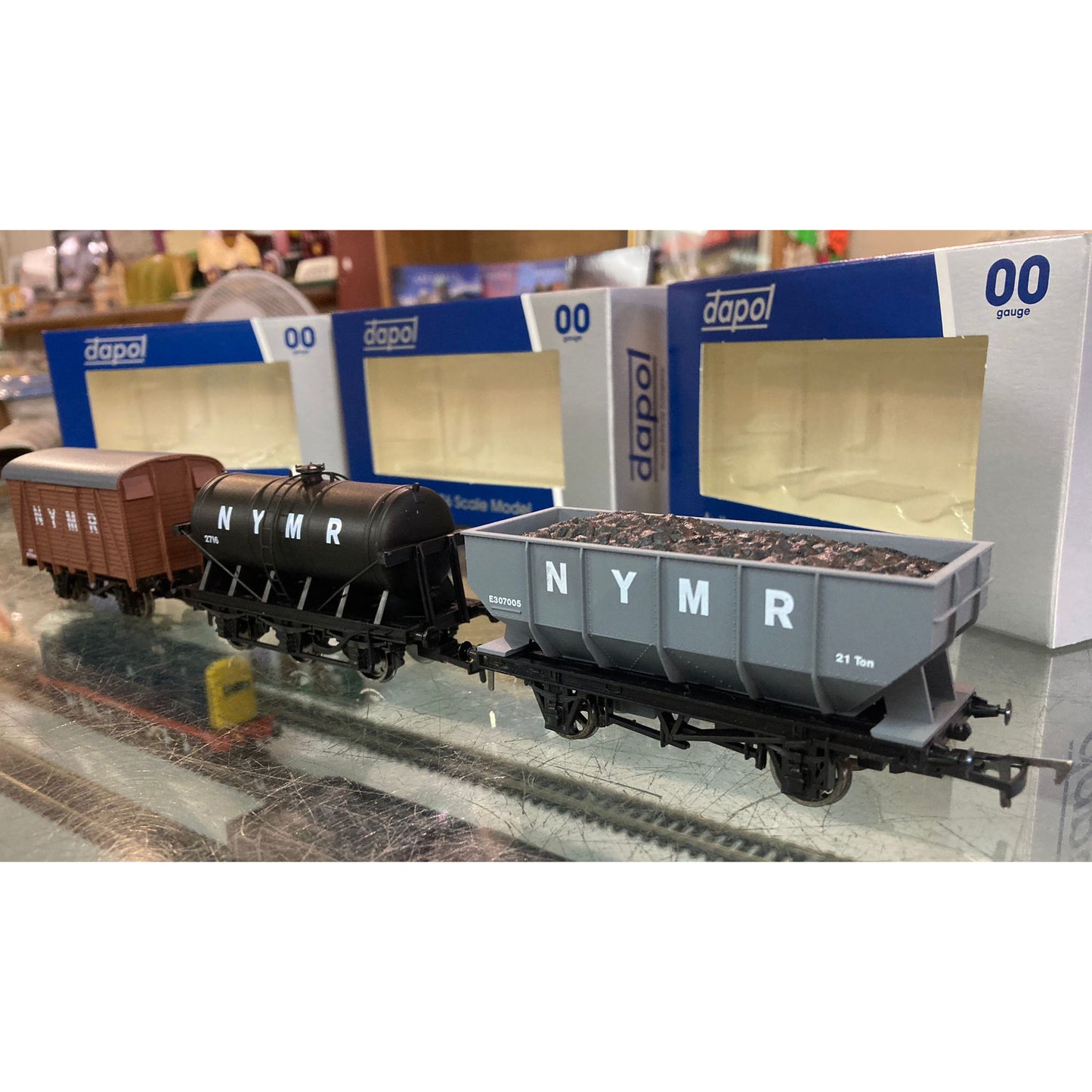 A line up of three different NYMR model wagons, the brown box van , black oil anker and grey hopper wagon. all coupled together on the glass shop counter in the Shed Shop.