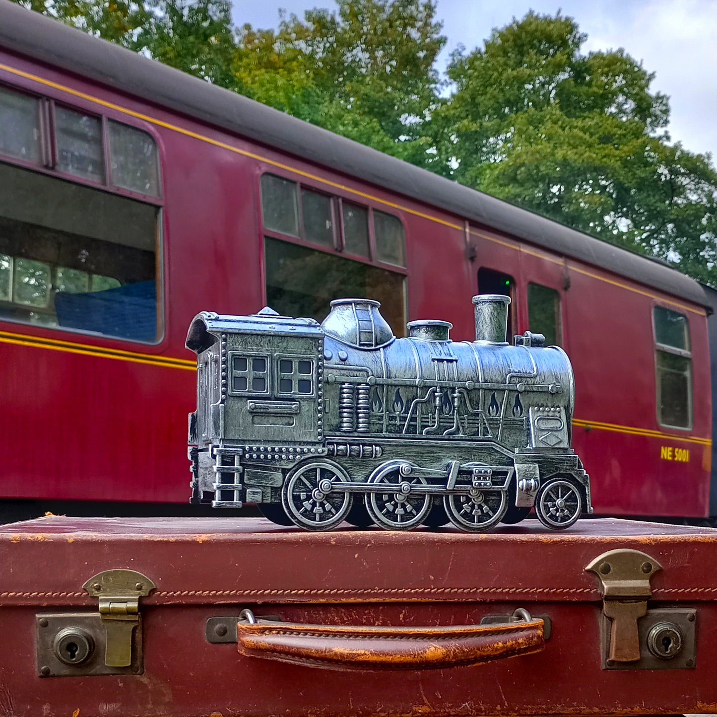 Silver train diffuser sat atop a vintage suitcase in front of a heritage train carriage
