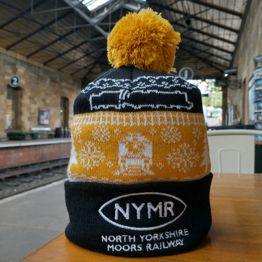 A knitted beanie hat in black, white and golden thread with a fabulous bobble on top. With train , rails and snowflake design and the NYMR logo on white on black on the front fold.