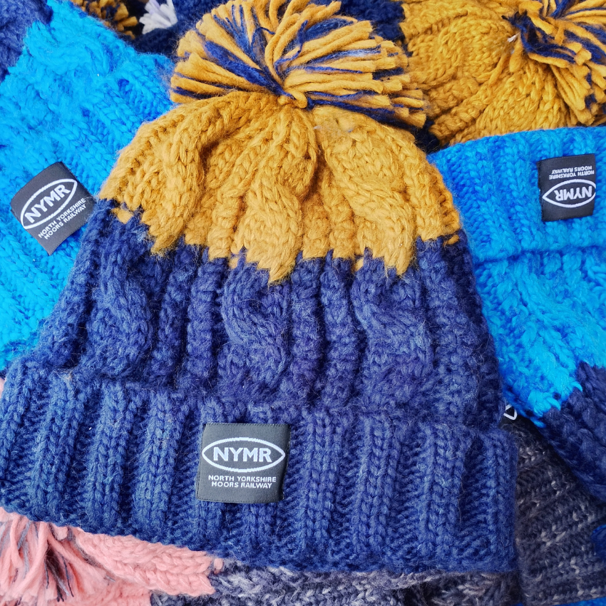 Knitted hats with pom-poms and NYMR labels on a blue background