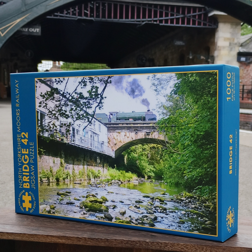 Jigsaw puzzle box featuring a scenic bridge and river with a blue border.