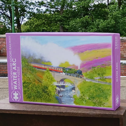 Jigsaw puzzle box with a train and landscape design on a wooden surface.