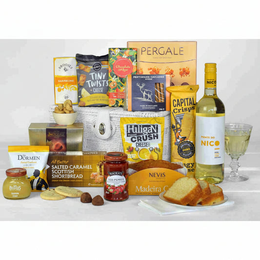 A bottle of white wine, savoury snacks, chocolates, biscuits, cake, preserves and a chutney in a black gift basket