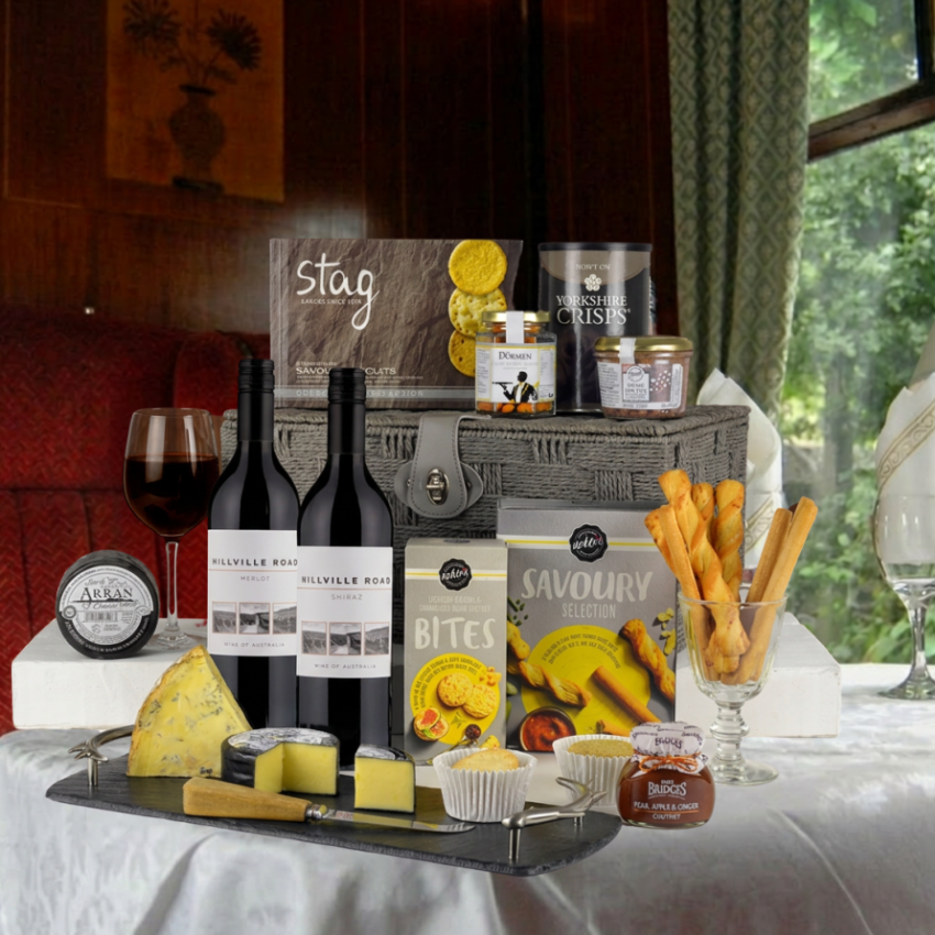 Gourmet gift basket with wine, cheese, and snacks on a table.