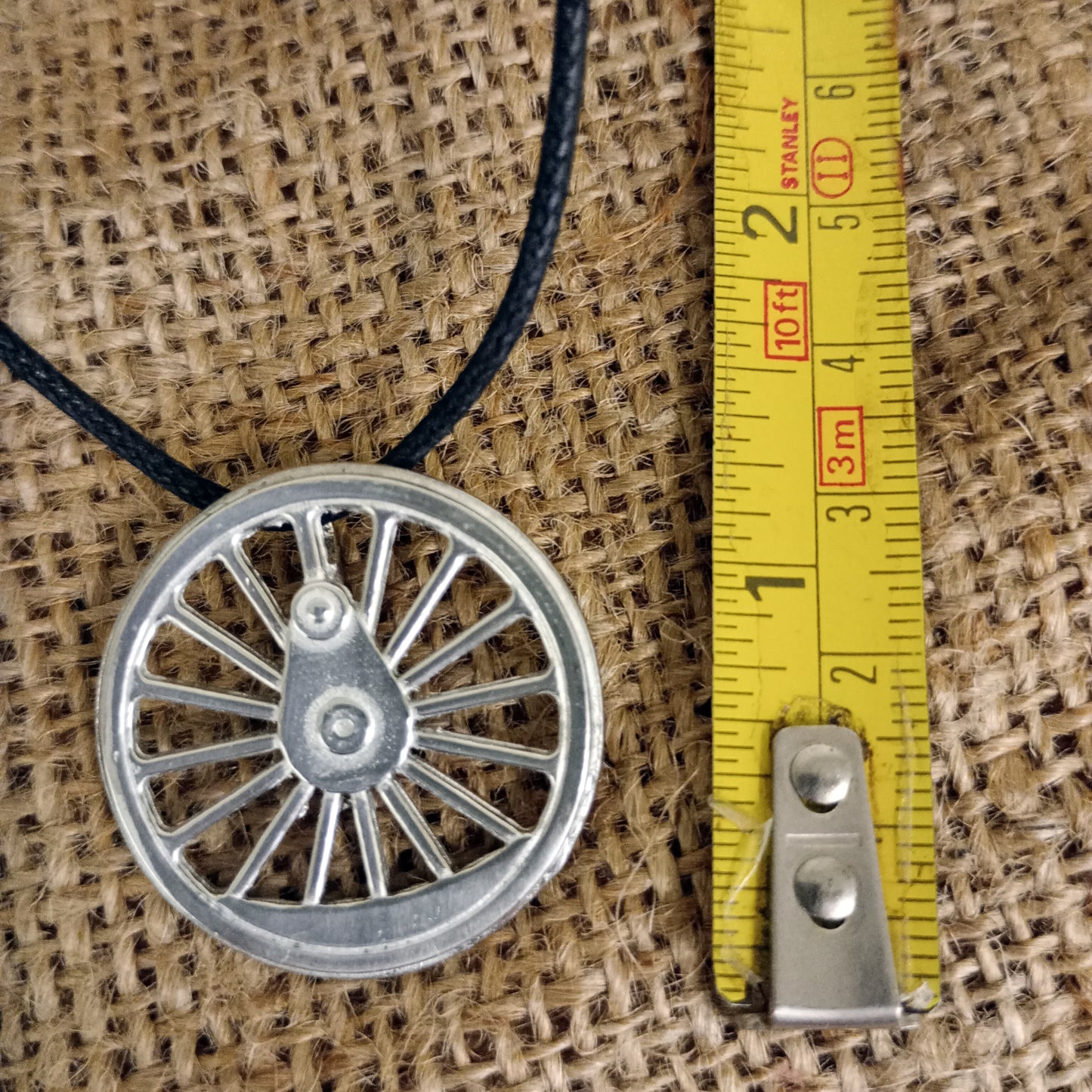 Pendant close up next to tape measure for scale - just over an inch diameter