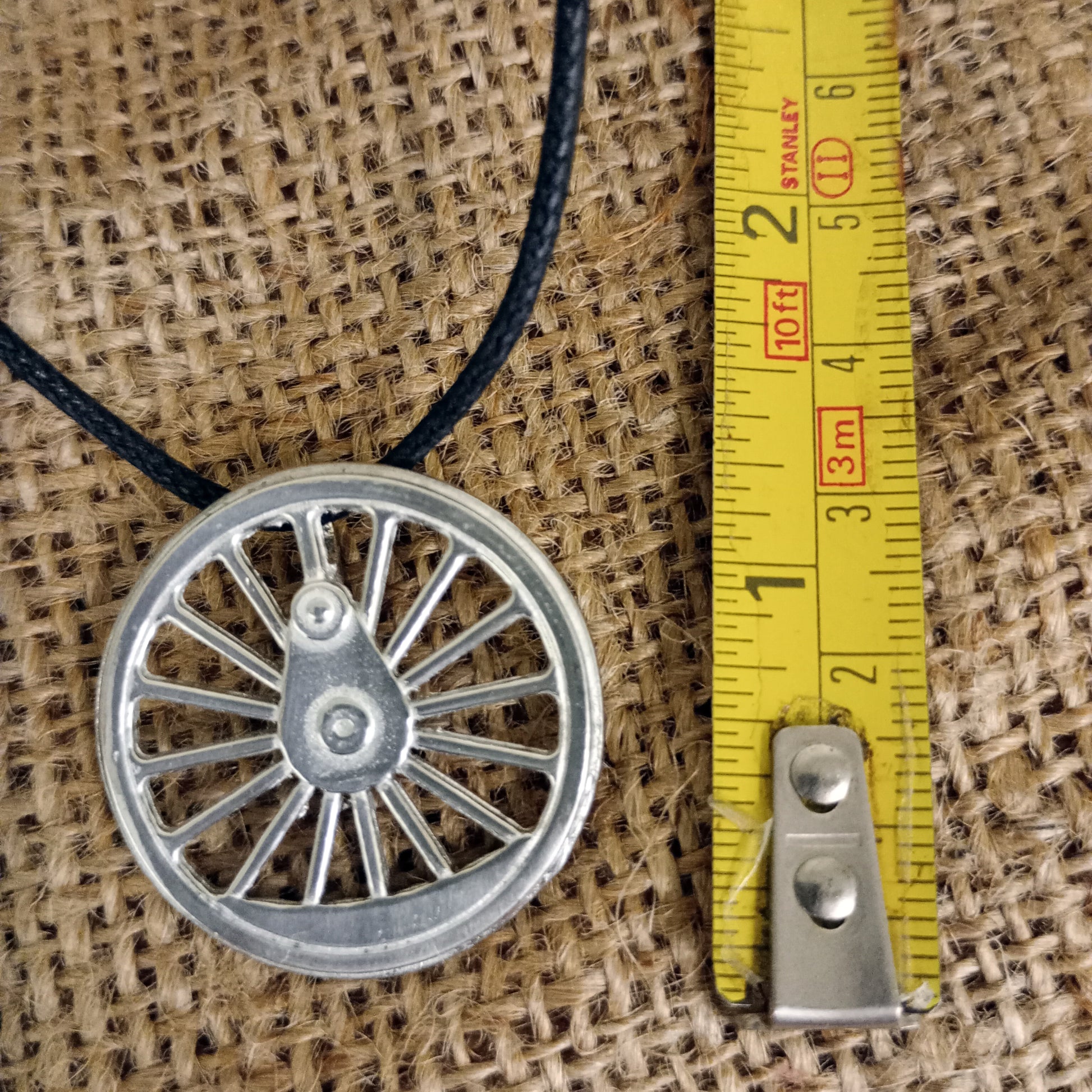 Pendant close up next to tape measure for scale - just over an inch diameter