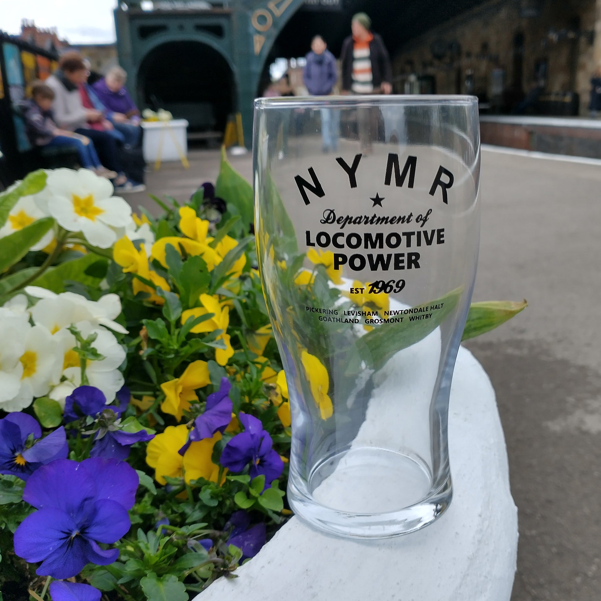 Tulip shaped pint glass with black N Y M R Locomotive Power logo and list of stations.
