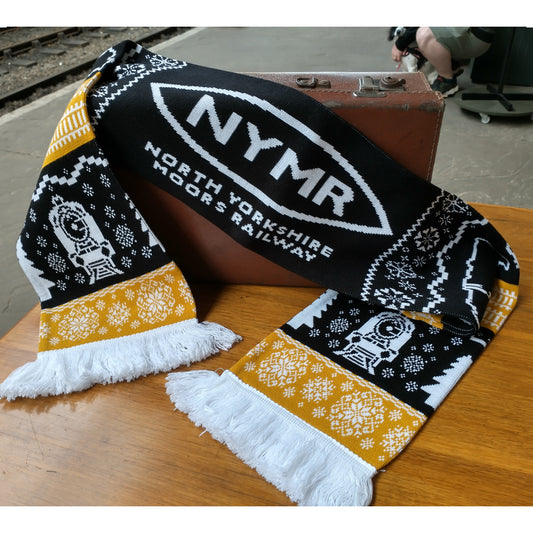 A knitted scarf in black, white and golden threads. With the NYMR logo in white on black, and loco details. Snowflakes and track motifs are white on a golden background.