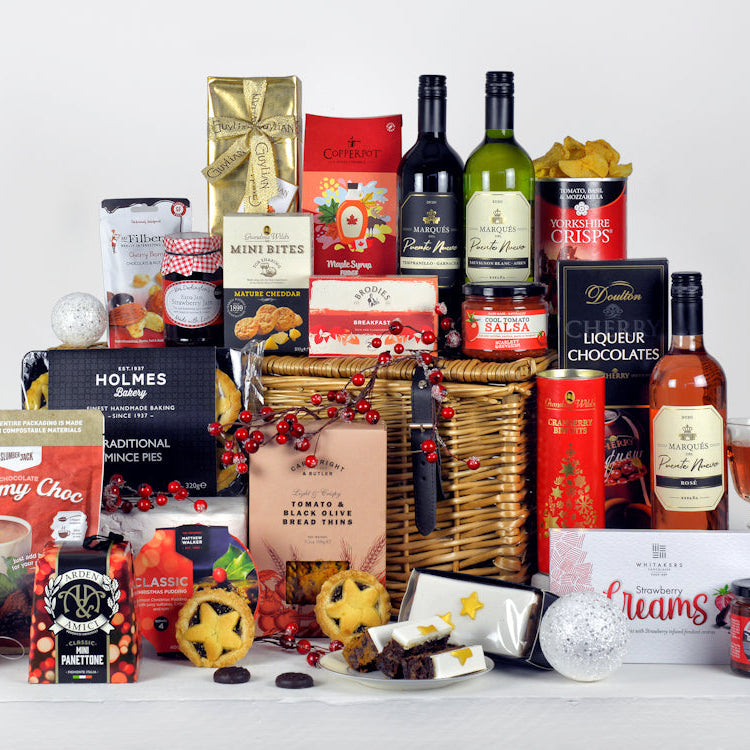 A selection of wines, Christmas pudding, mince pies, biscuits, chocolates and other tasty festive food in a wicker basket.