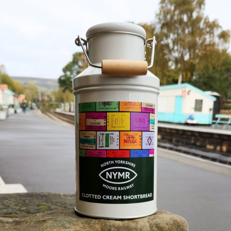 A cream coloured metal churn shaped tin with NYMR logo and ticket design, pictured on Grosmont Station