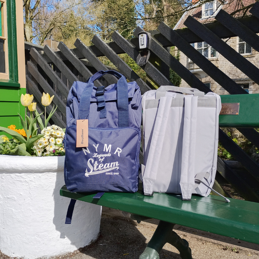 Blue backpack with 'NMR Legends of Steam' branding on a green bench outdoors.