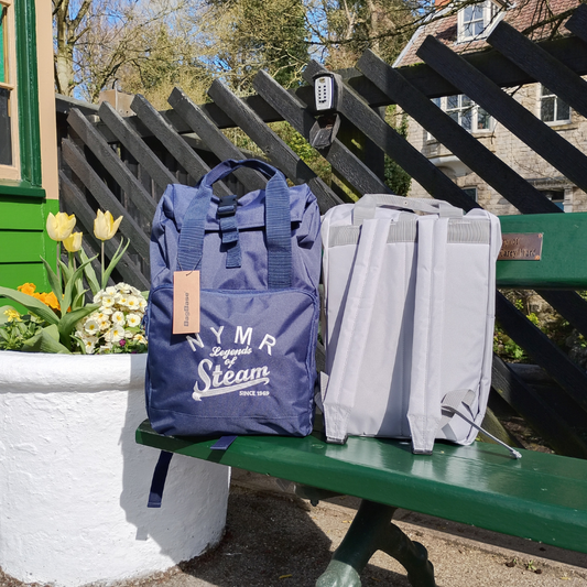 Blue backpack with 'NMR Legends of Steam' branding on a green bench outdoors.