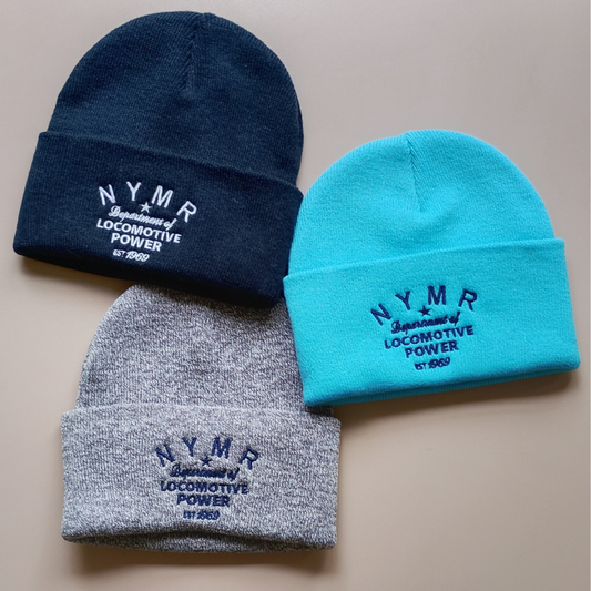 Three knit beanie hats arranged on a plain beige background: one dark navy, one bright aqua/turquoise, and one heather gray. Each hat has folded cuff embroidery reading “NYMR Department of Locomotive Power” with a small “EST 1969” detail.