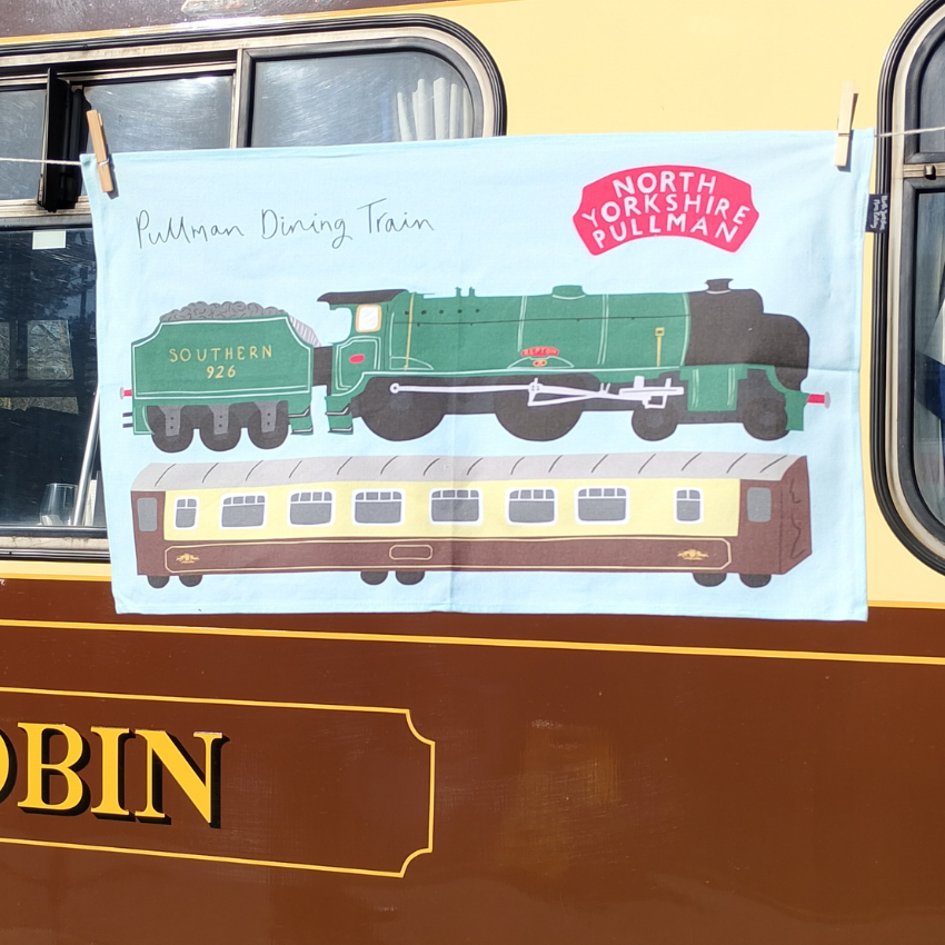 Tea towel with train design and 'North Yorkshire Pullman' branding hanging in front of the dining carriage.