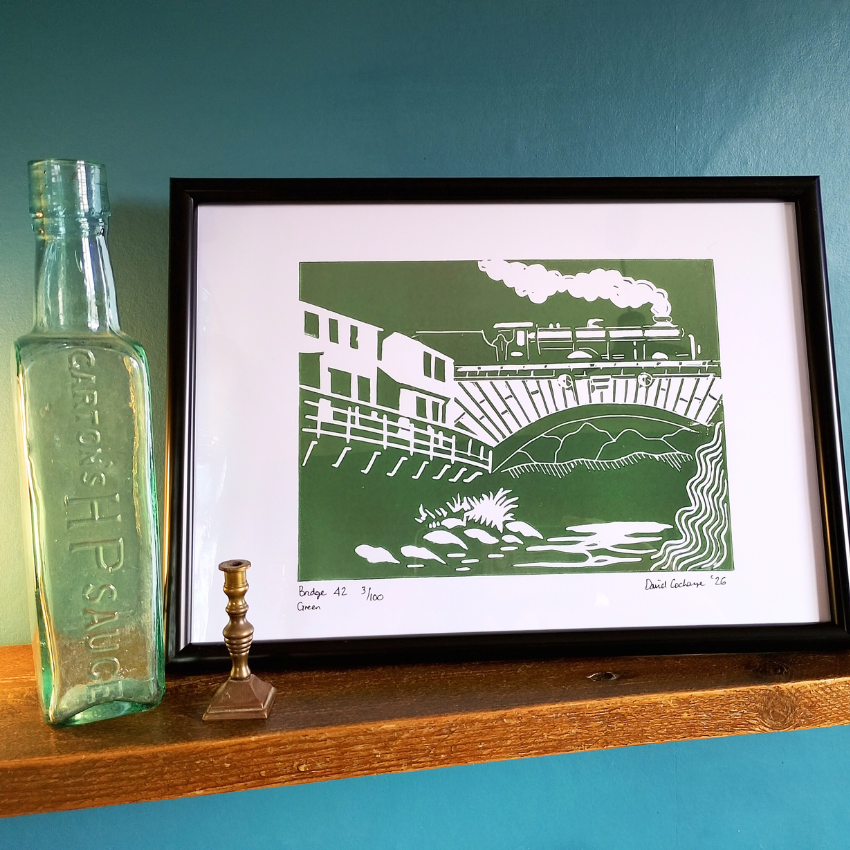Framed artwork of a train on a bridge with a bottle and candlestick on a shelf.