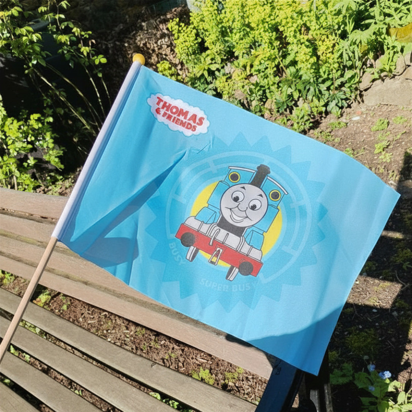 Blue flag with Thomas the Tank Engine design on a wooden bench outdoors.