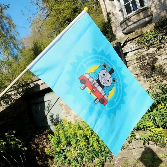 Blue flag with a cartoon train character in front of a stone building and greenery