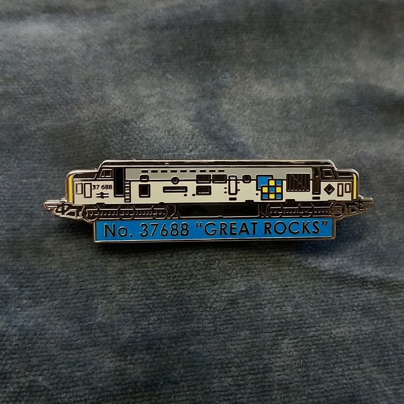 An enamel pin shaped like a locomotive train, featuring a two tone grey body with a blue section at the bottom that reads 'No. 37688 "GREAT ROCKS"' in yellow lettering.