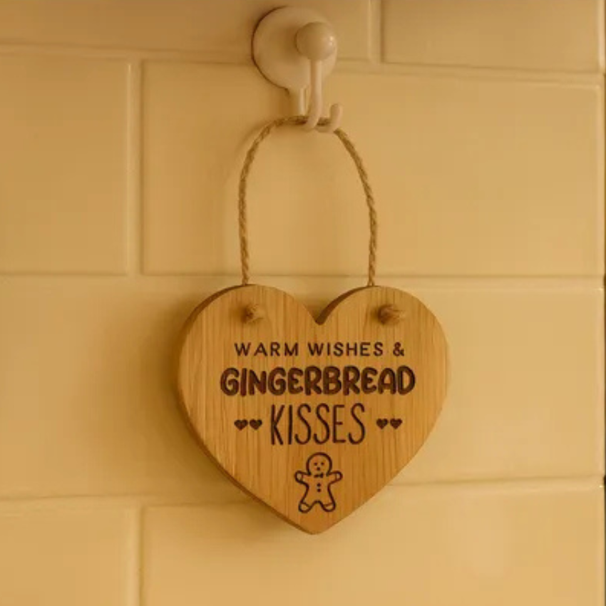 Wooden heart-shaped sign with text 'Warm wishes & Gingerbread kisses' hanging on a wall.