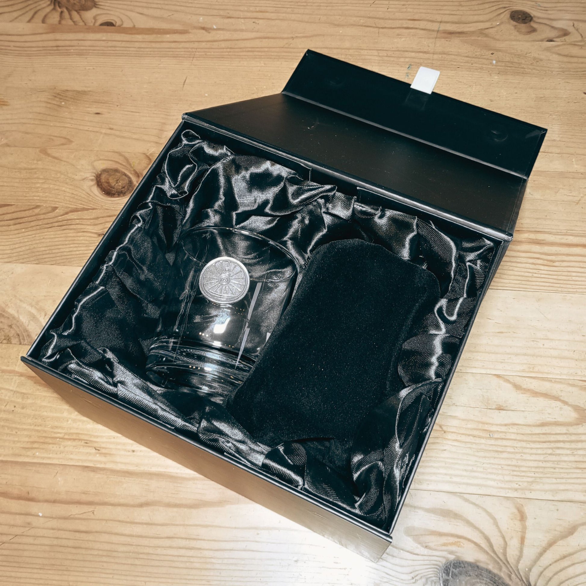 A whisky glass nestled inside a lined gift box alongside its mate, which is still hiding inside its velvet pouch.