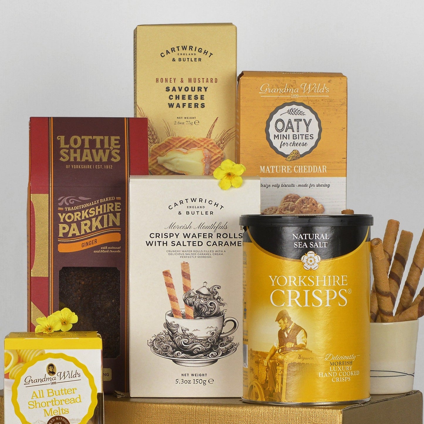 A curated gift basket of Yorkshire treats and teas, featuring boxes and tins of Lottie Shaws, Cartwright & Butler, and Grandma Wilds, arranged on a gold tray against a neutral light gray background.