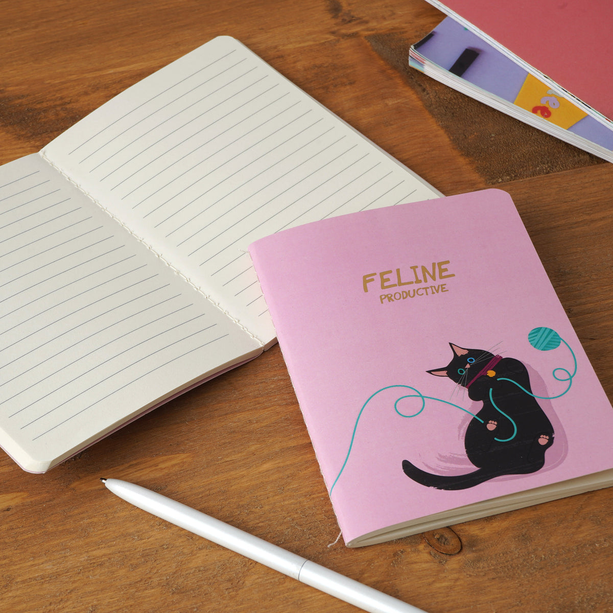 The pink notebook on a wooden desk with an open notebook showing lined pages next to it.