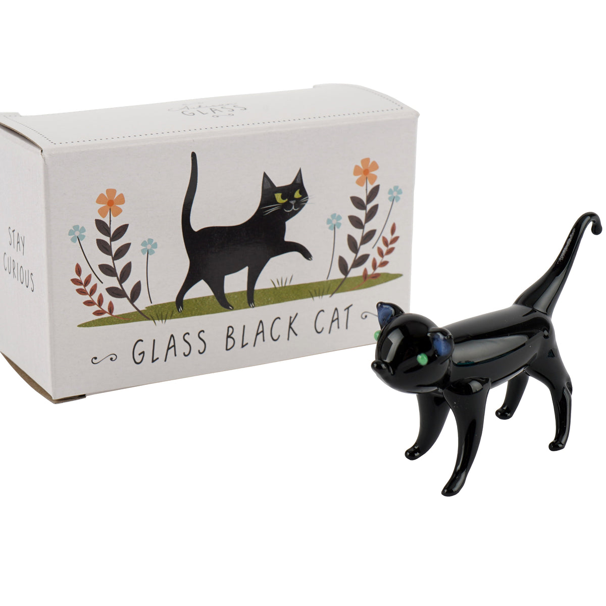 A glass ornament of a black cat with tail high and curved and green eyes, positioned in front of an illustrated card gift box.