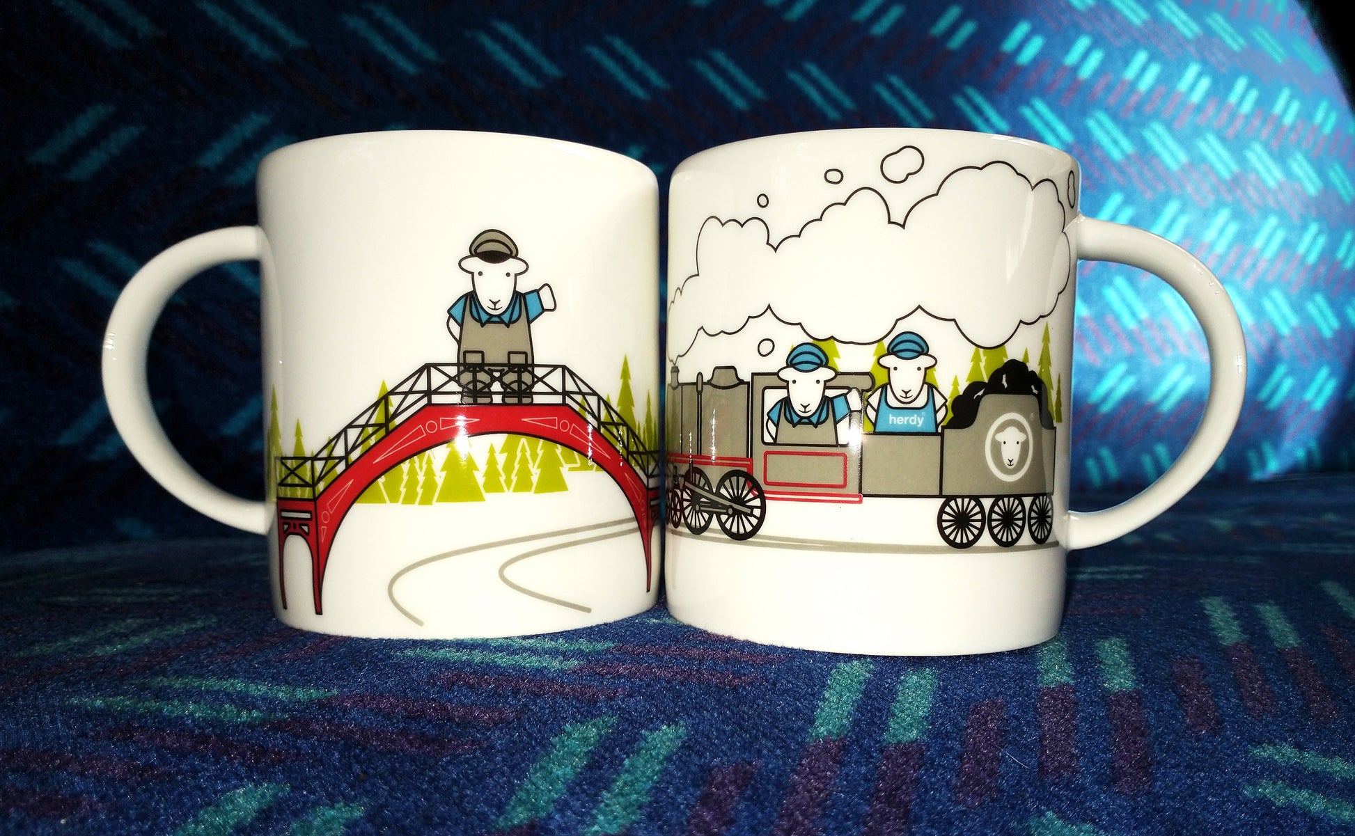 Both sides of white Herdy Mug with coloured cartoon of Herdy on footbridge on one side and two Herdys driving steam engine on the other