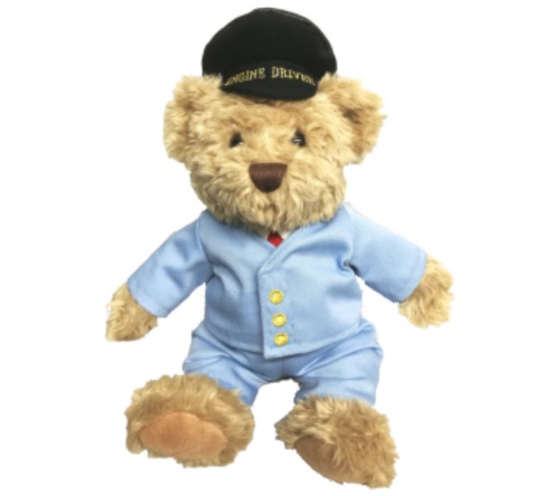 Gold coloured teddy bear in pale blue suit wearing black cap with Engine Driver written on peak