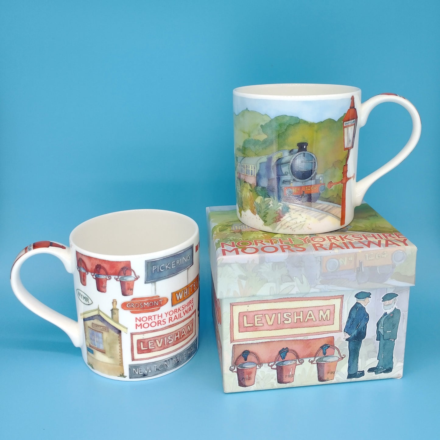 White mug with painting of steam train and old street light on front and various railway signs, etc . on back. With presentation box with the same pictures and North Yorkshire Moors Railway printed on top
