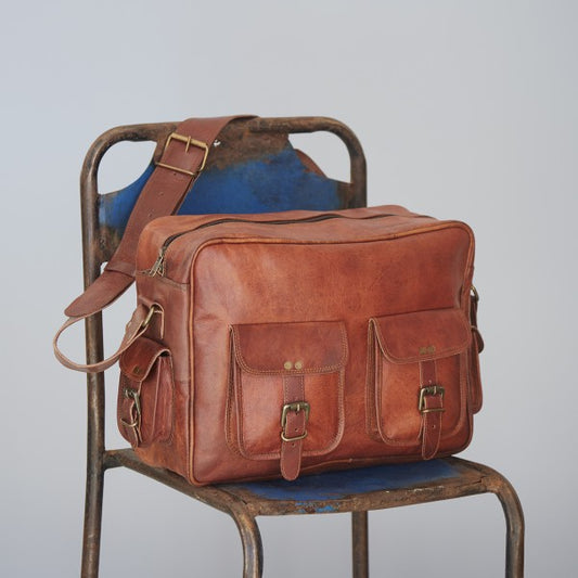 Tan leather travel bag with wide strap, zip top and pockets with buckle fastenings.