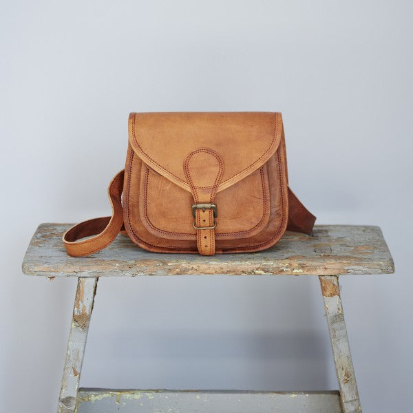 Small tan leather shoulder bag with extra pocket on front and flap with buckle fastening.